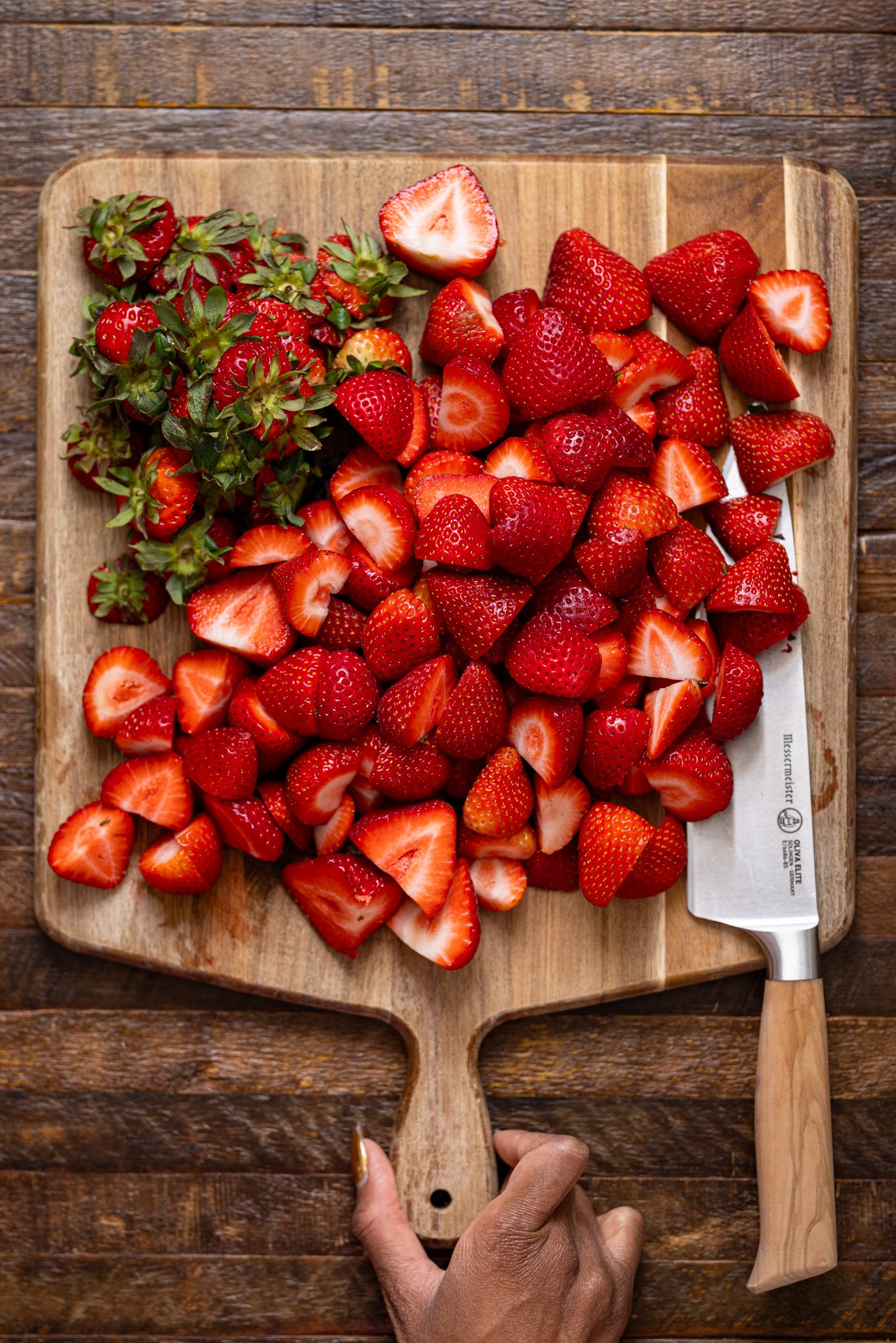 Chopped strawberries on a cutting board with a knife.