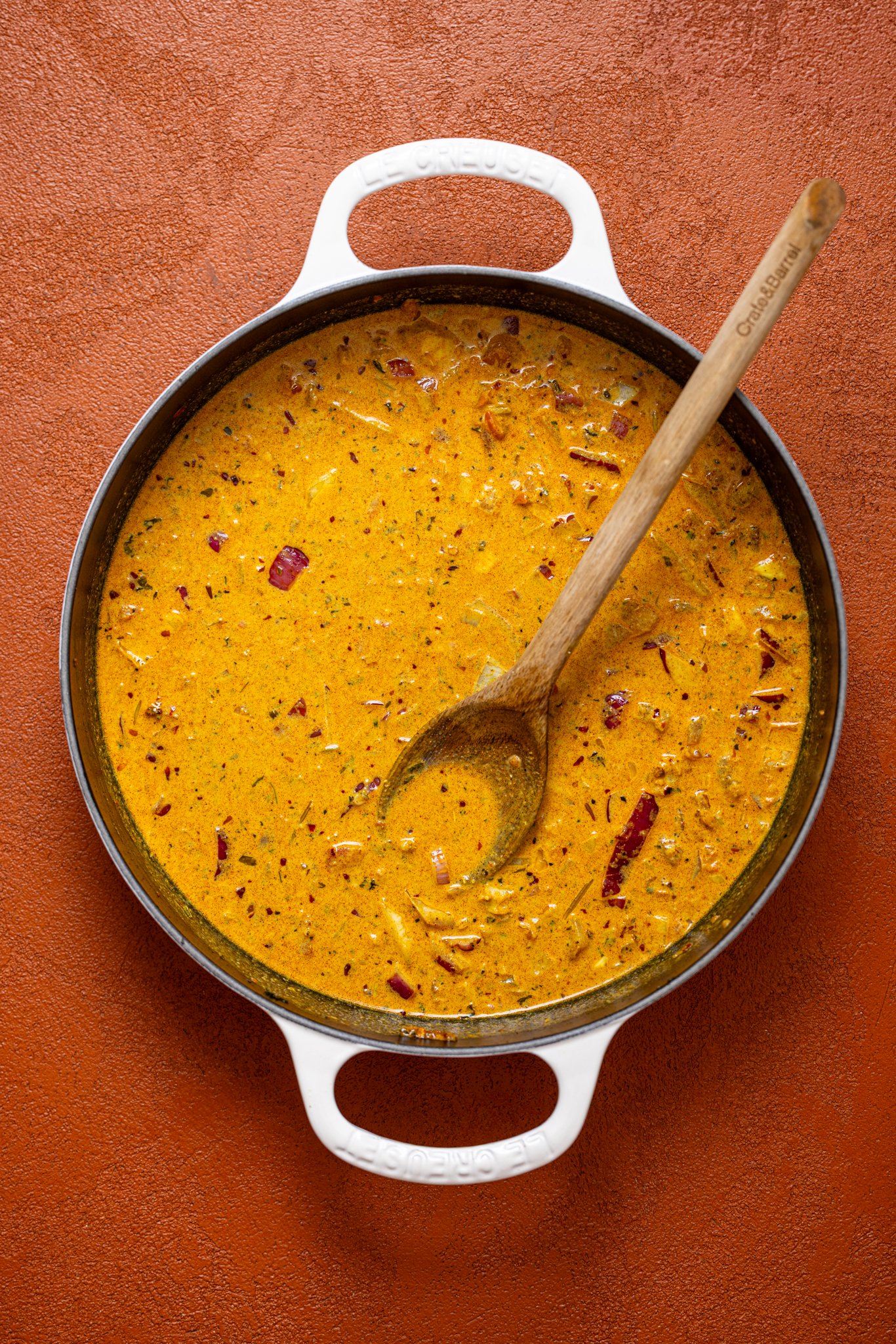Butter chicken sauce in a skillet with a wooden spoon.