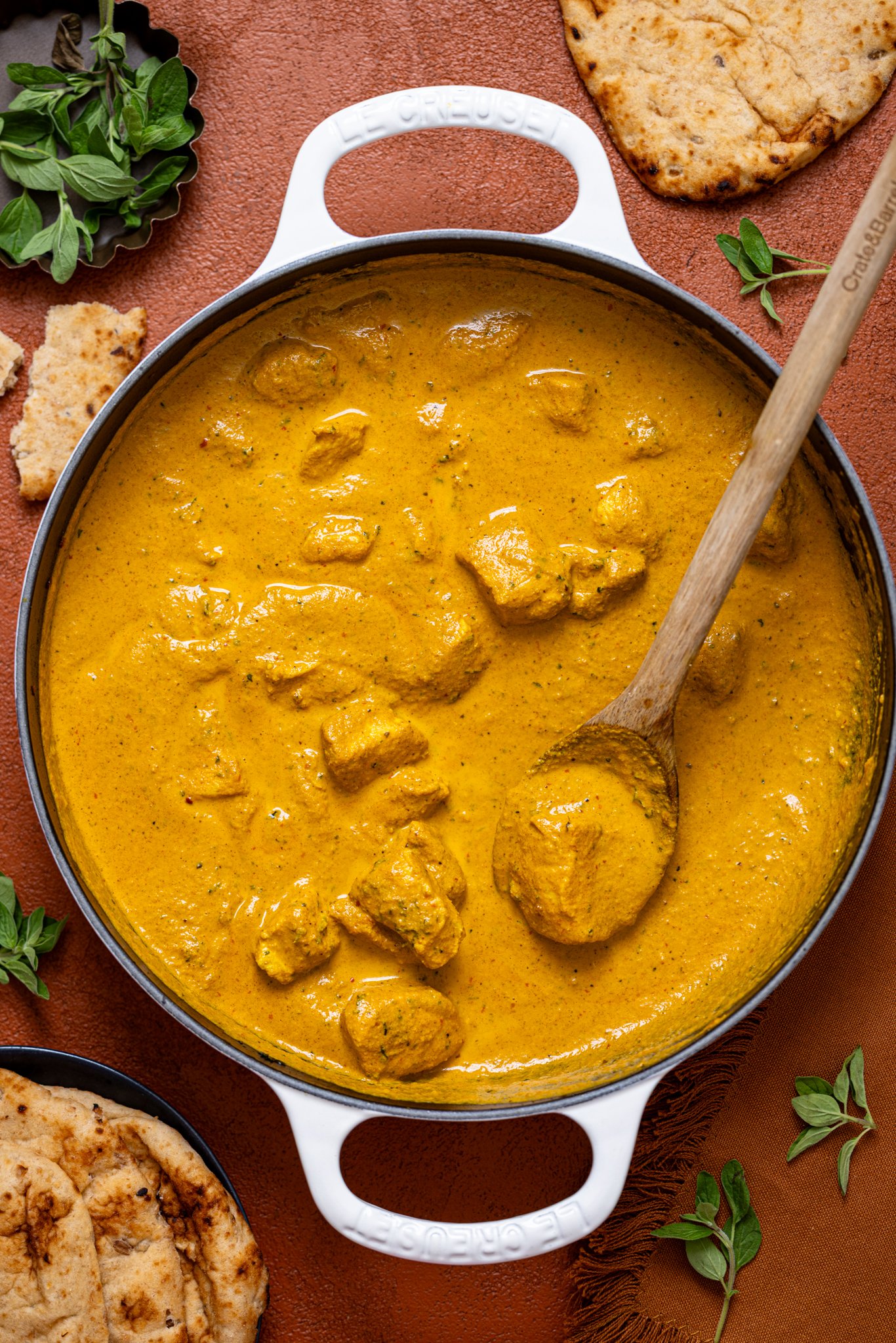 Spicy Butter Chicken in a skillet with a wooden spoon and naan bread.
