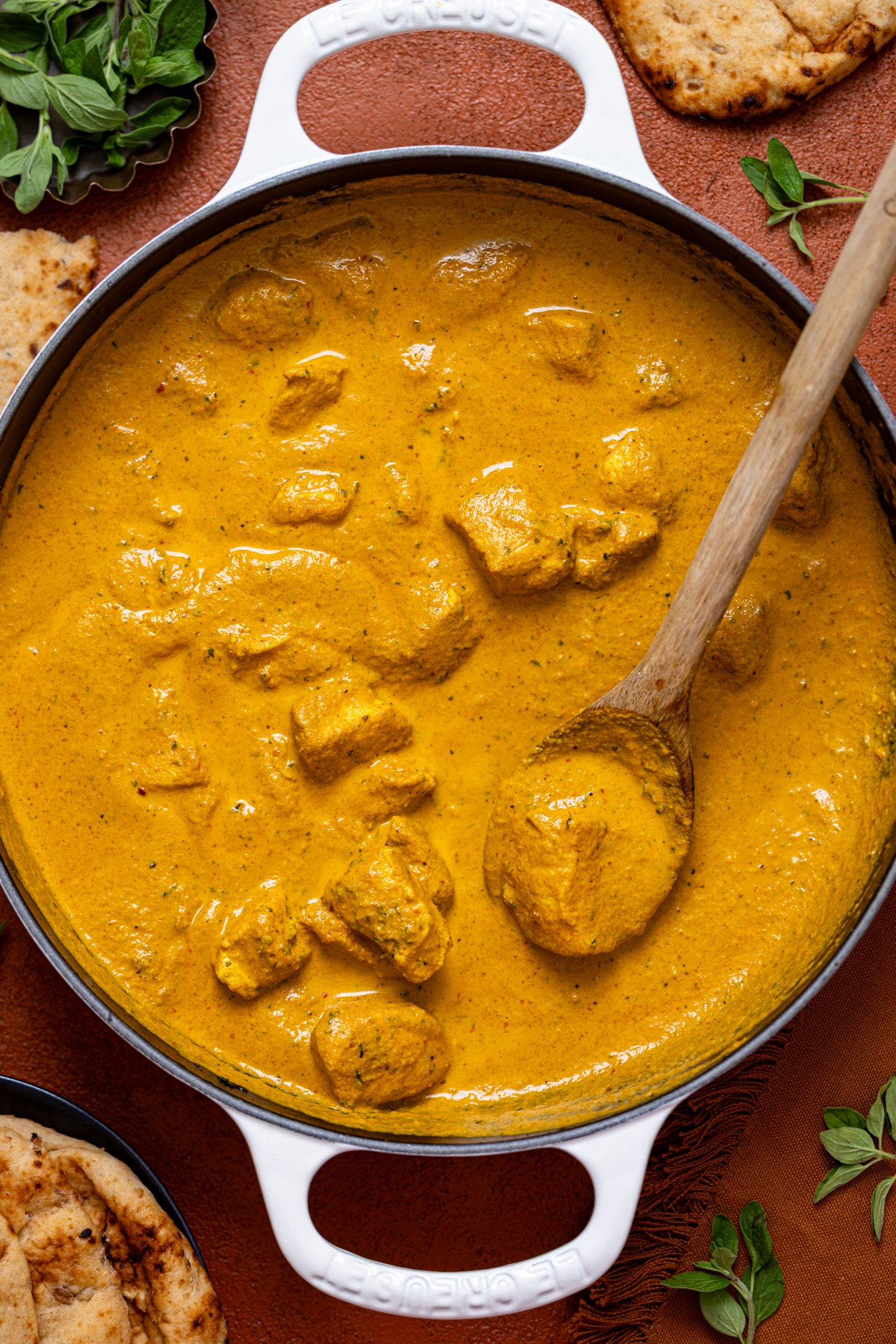 Spicy Butter Chicken with naan bread and a wooden spoon.
