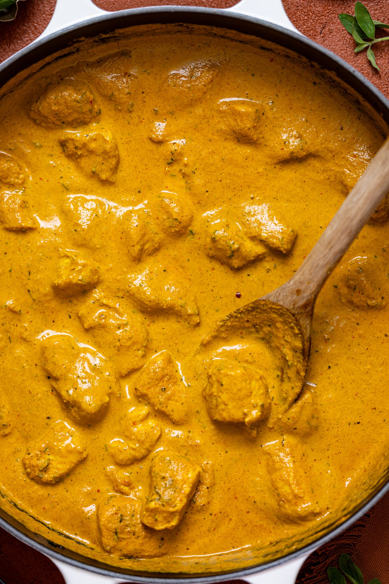 Up close shot of spicy butter chicken in a skillet with a wooden spoon.