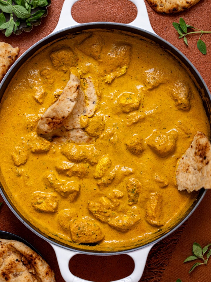 Spicy Butter Chicken in a white skillet with naan bread.
