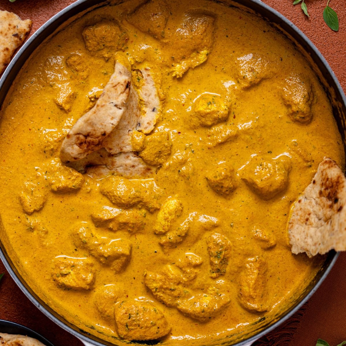 Spicy Butter Chicken in a white skillet with naan bread.