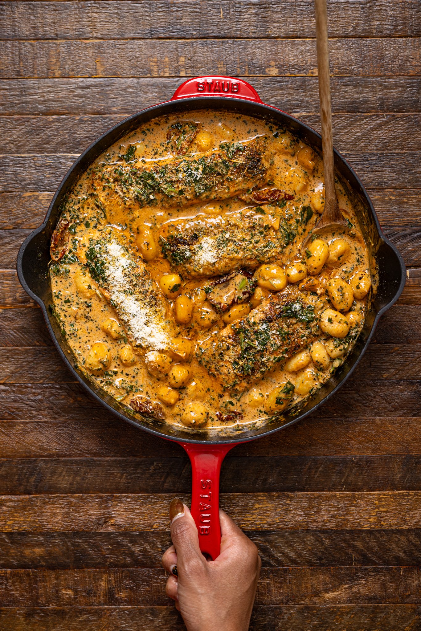 The Best Tuscan Marry Me Salmon in a red skillet with a spoon being held by woman hands.