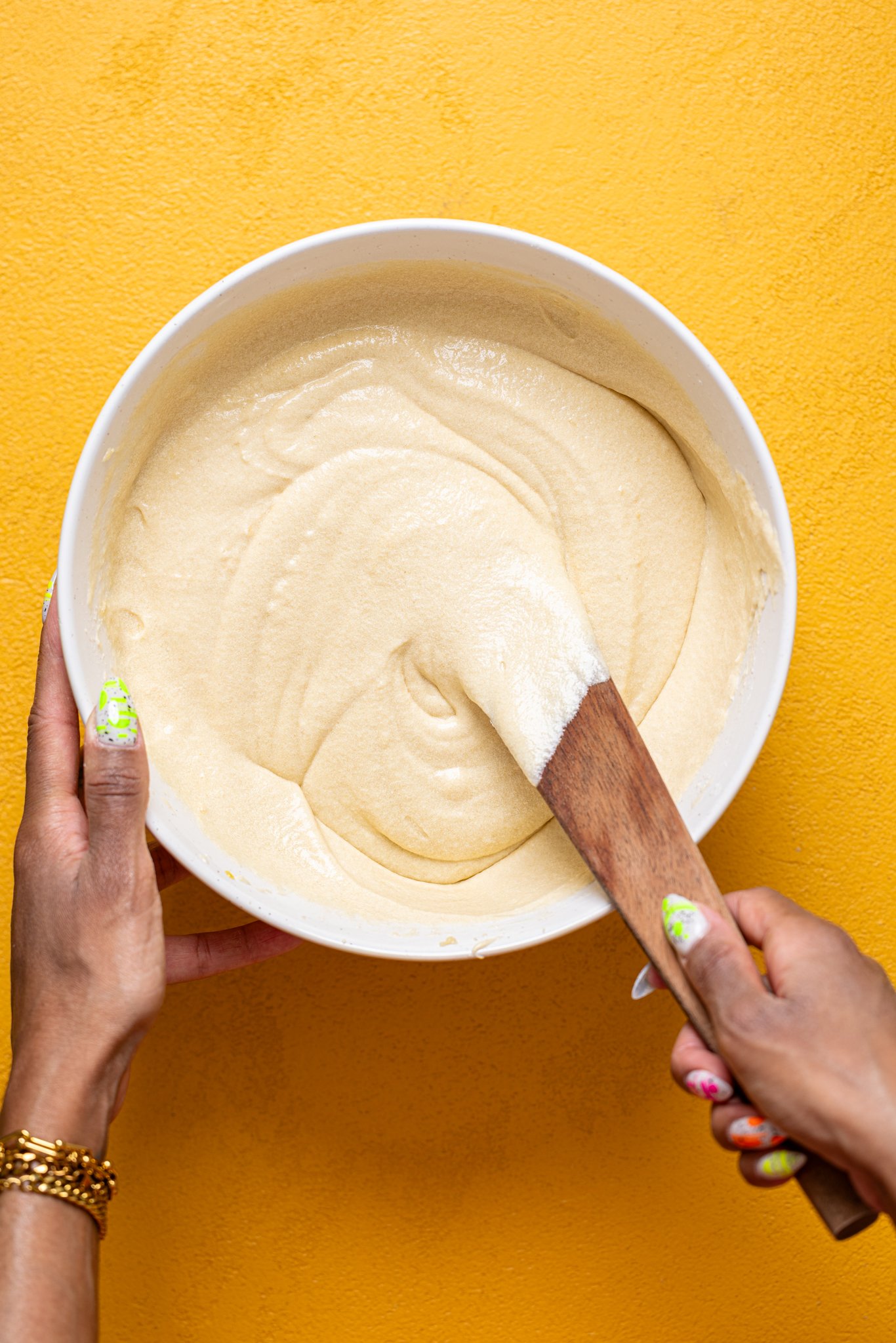 Woman hands mixing together batter with a wooden spoon.
