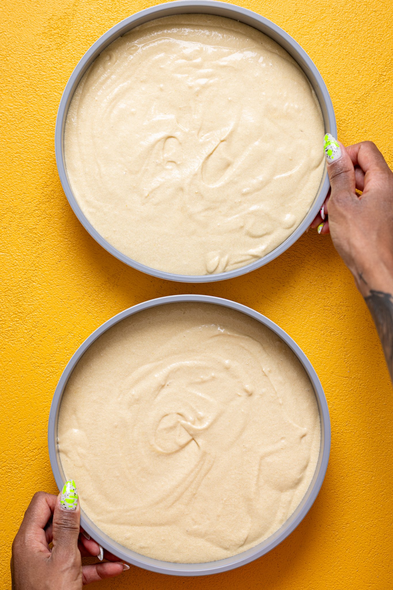 Woman hands holding two cake pans filled with batter.