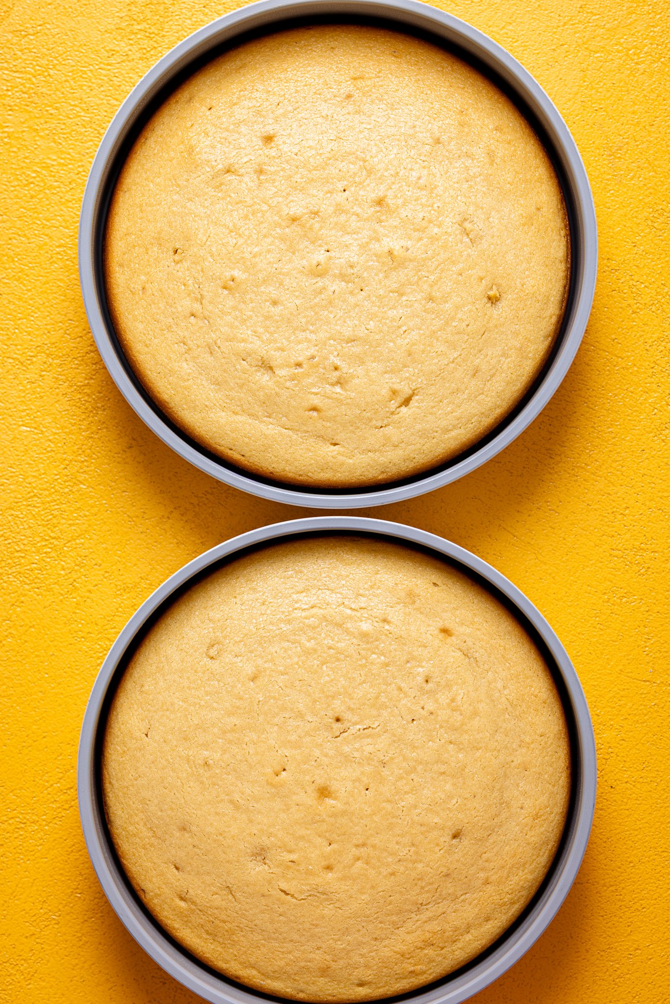 Baked cakes in cakes pans on a yellow table.