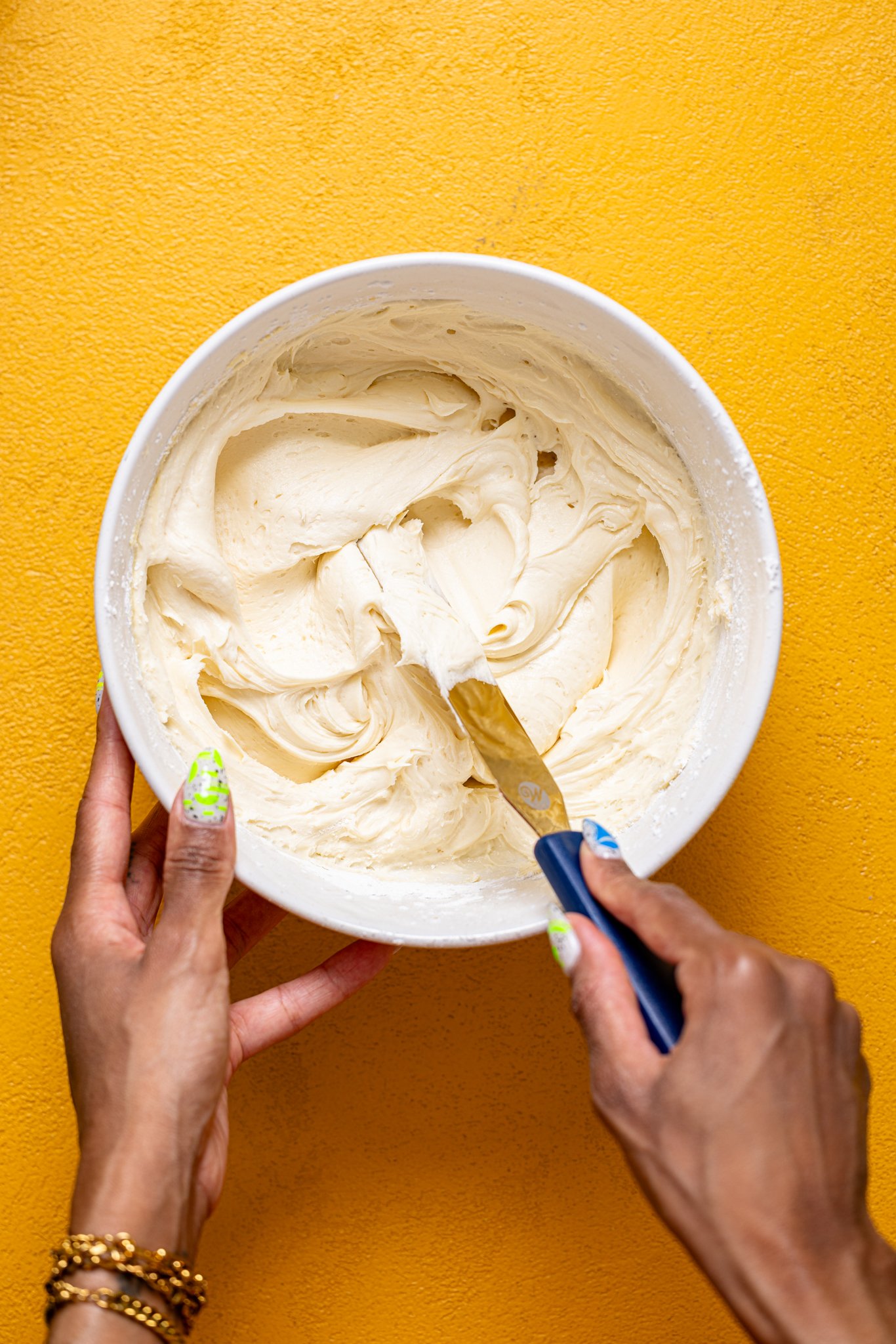 Woman hands mixing buttercream in a bowl with a spatula.