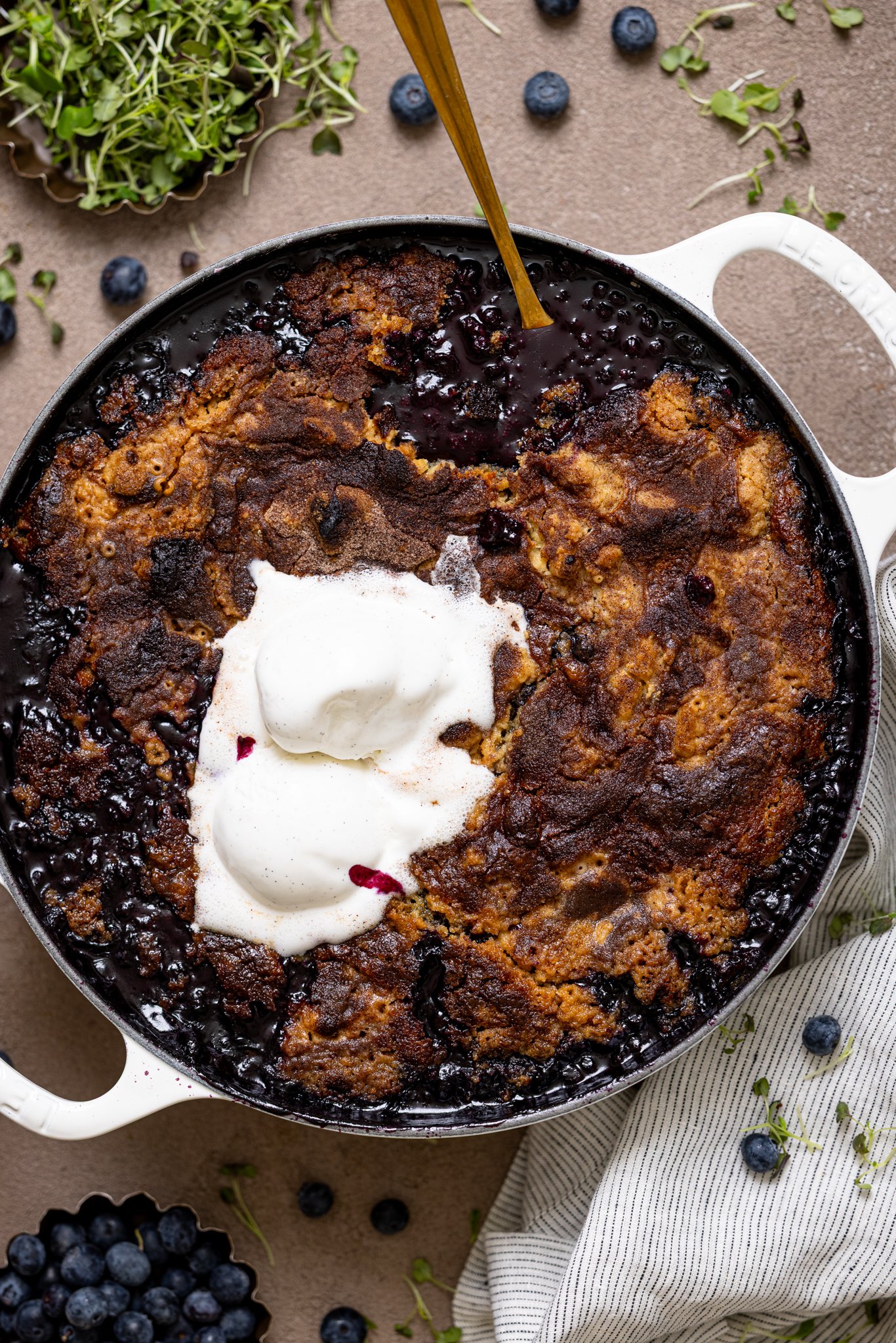 My Fave Blueberry Dump Cake in a white skillet with a spoon and blueberries.