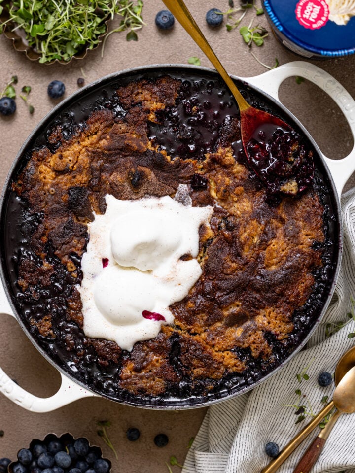 My Fave Blueberry Dump Cake in a white skillet with a spoon and ice cream.