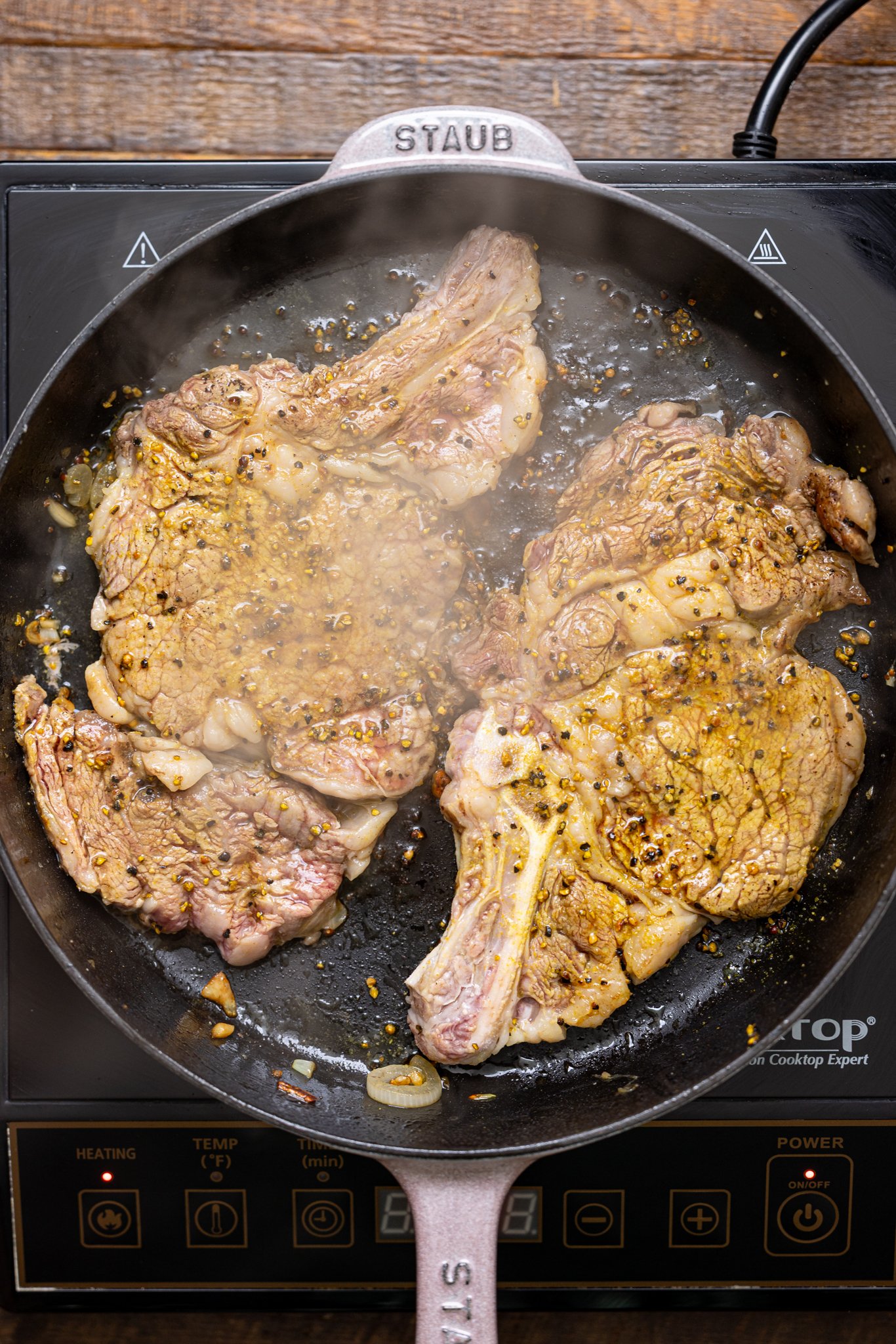 Steak being seared in a skillet over the stovetop.
