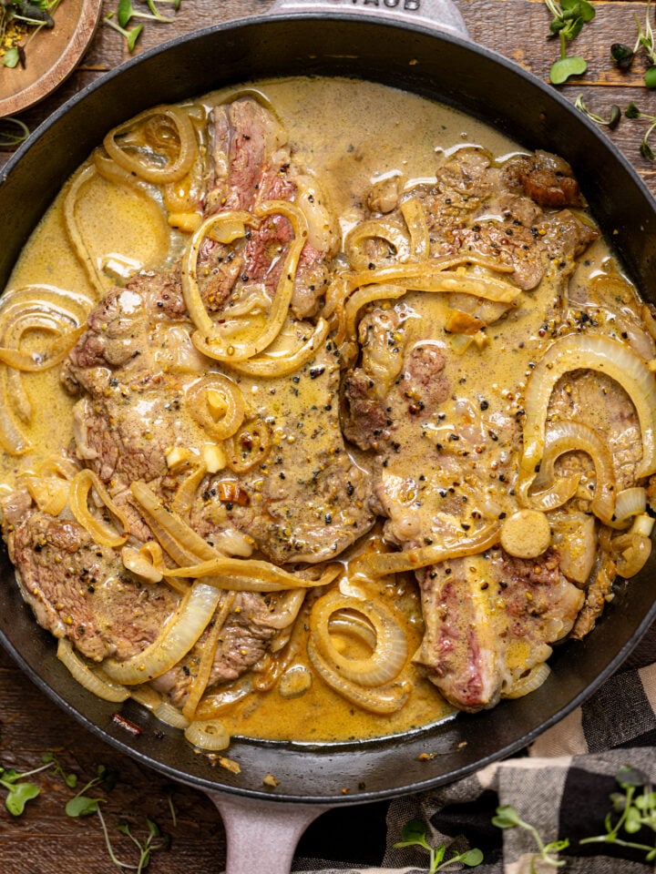 The Best Southern Smothered Steak in a skillet on a brown wooden table.