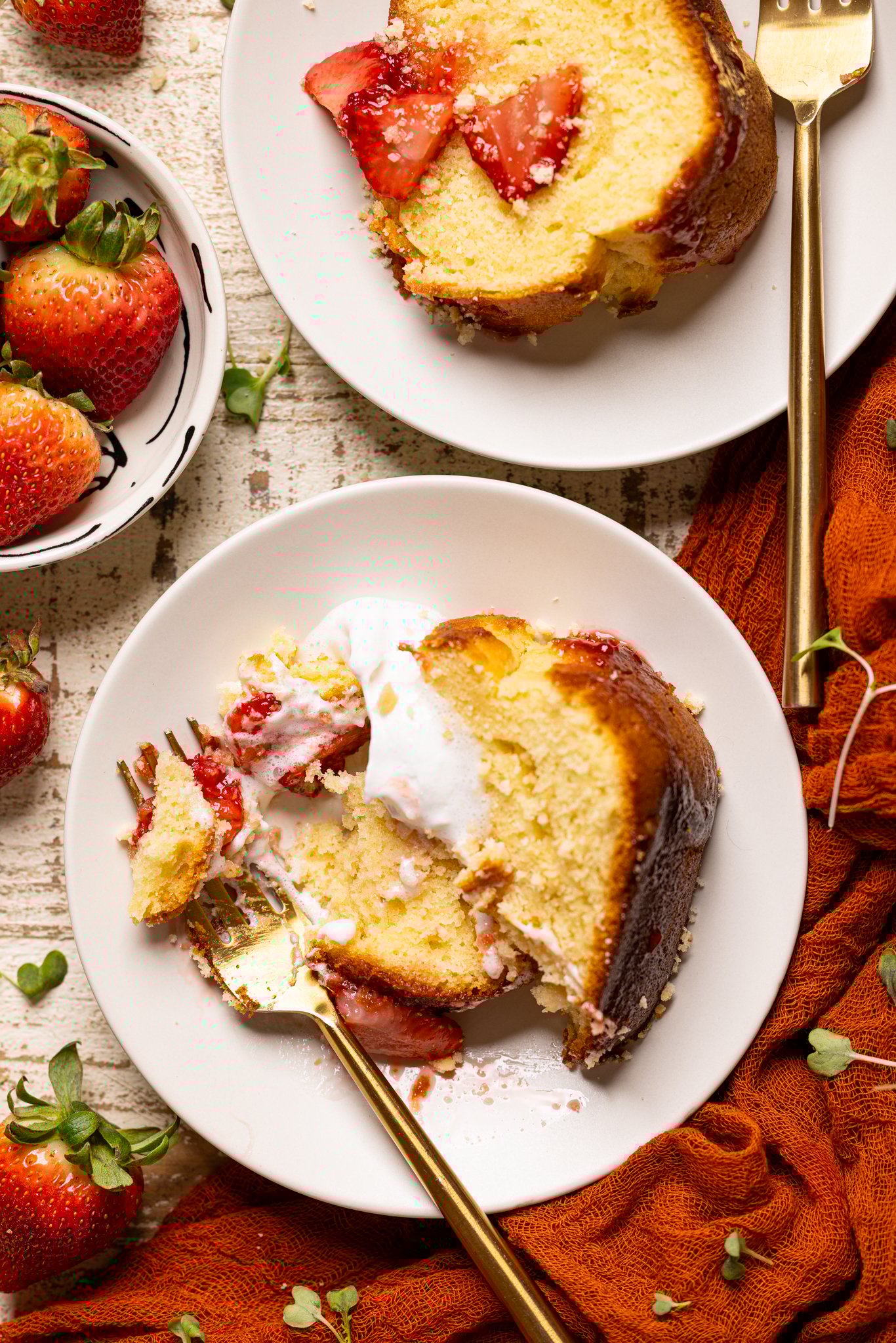 A slice of Strawberry Shortcake Bundt Cake on a plate with a fork and whipped cream.