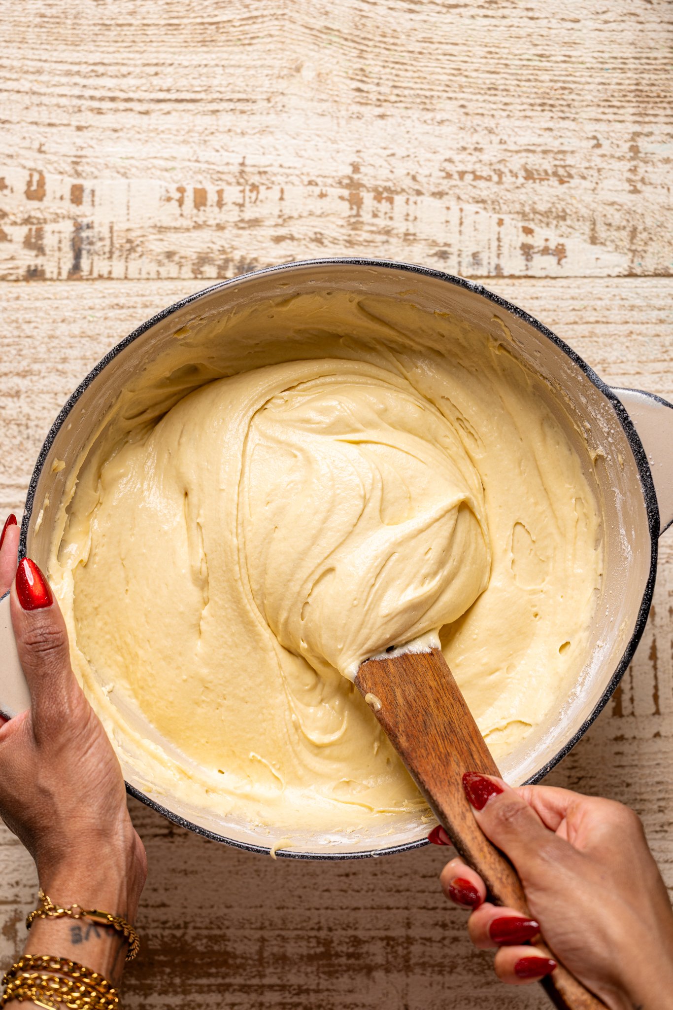Cake batter in a bowl being mixed with a wooden spoon by woman hands.