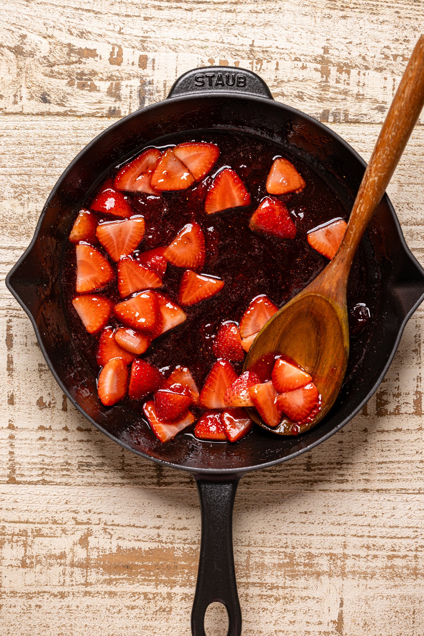 Sautéed strawberry topping in a skillet with a wooden spoon.