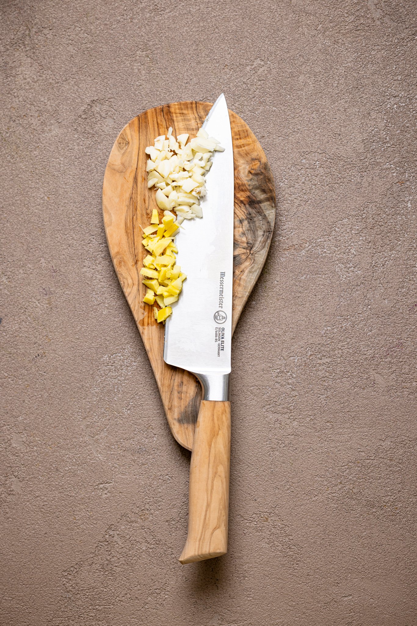 Minced garlic with a knife on a small cutting board.