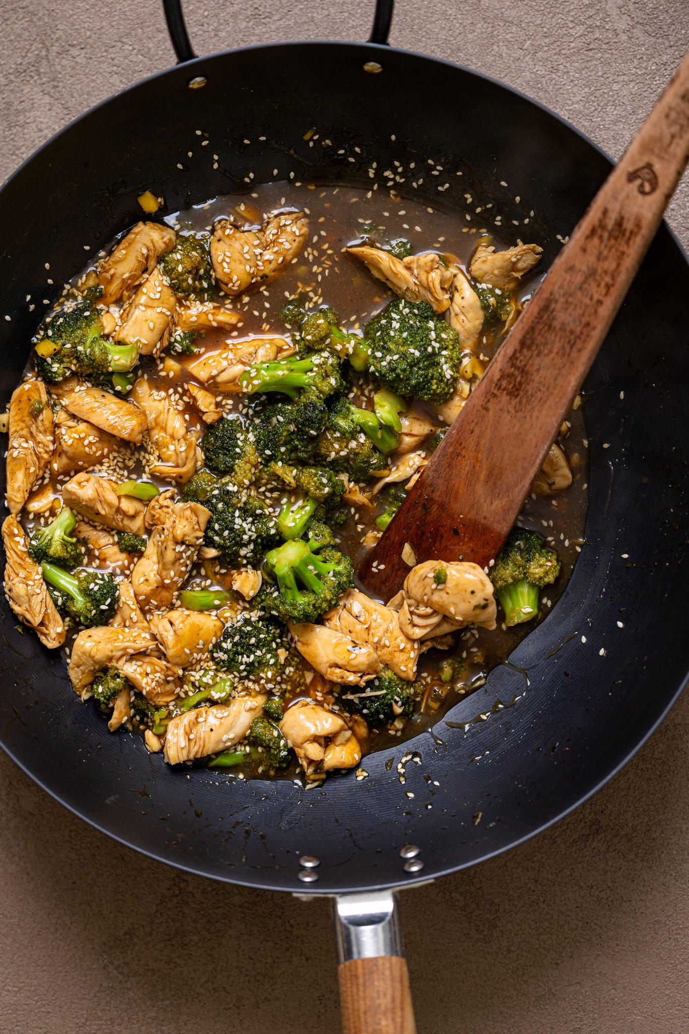 Ingredients simmering in wok with a wooden spoon.