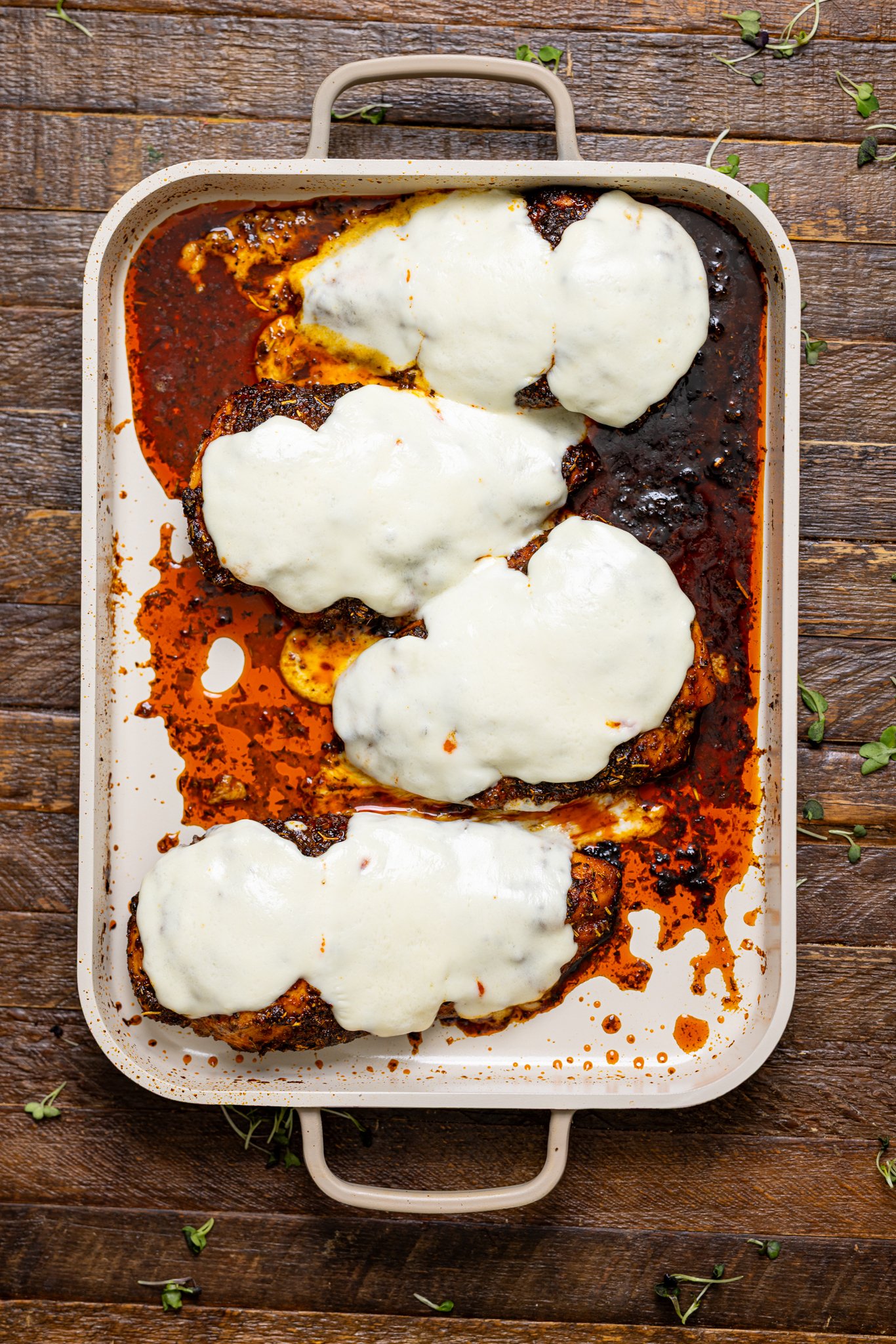 Baked chicken breasts topped with mozzarella cheese on a baking griddle.