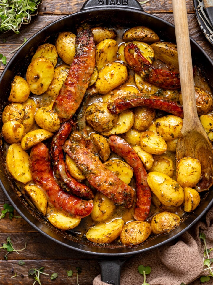Baked Andouille Sausage + Potatoes with a wooden spoon in a skillet.