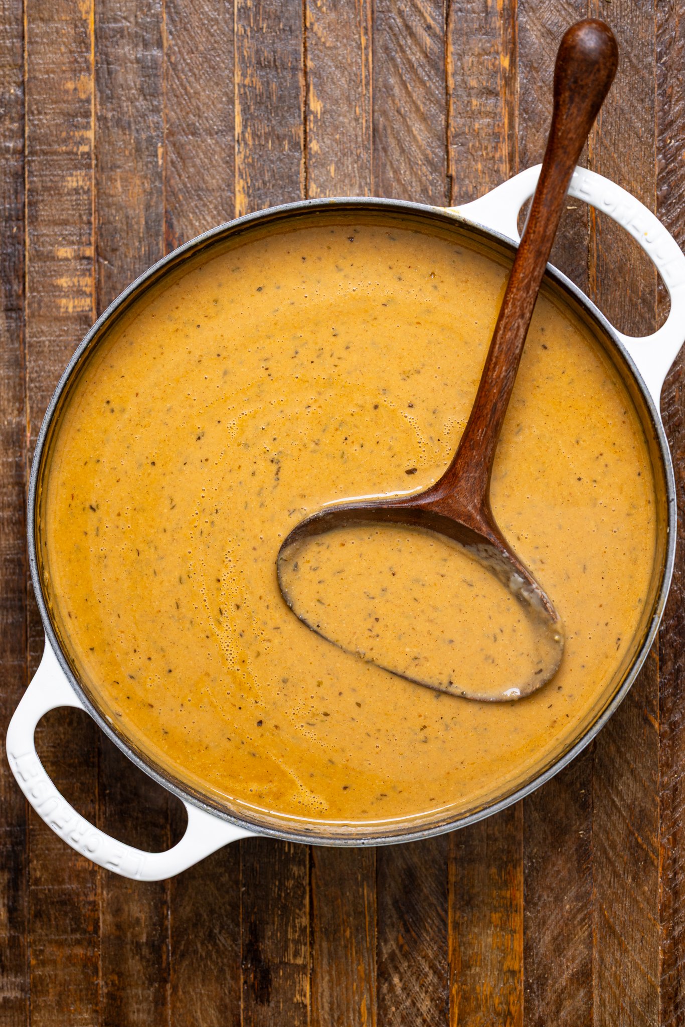 A pot of Creamy Roasted Apple Pumpkin Soup with a wooden spoon.