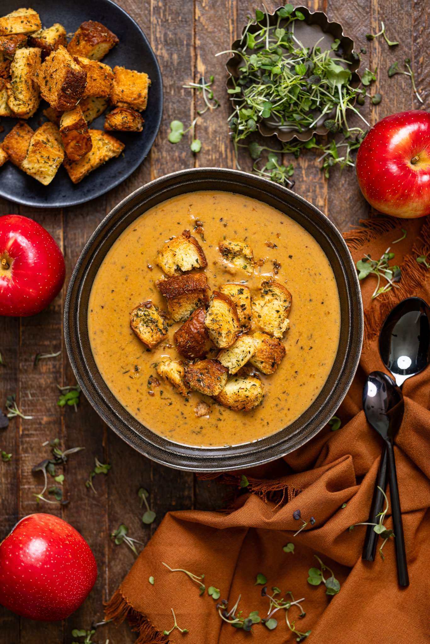 Creamy Roasted Apple Pumpkin Soup in a bowl with spoon and apples.