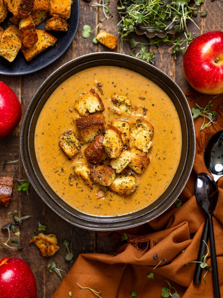 Creamy Roasted Apple Pumpkin Soup in a bowl with spoons with croutons and apples.