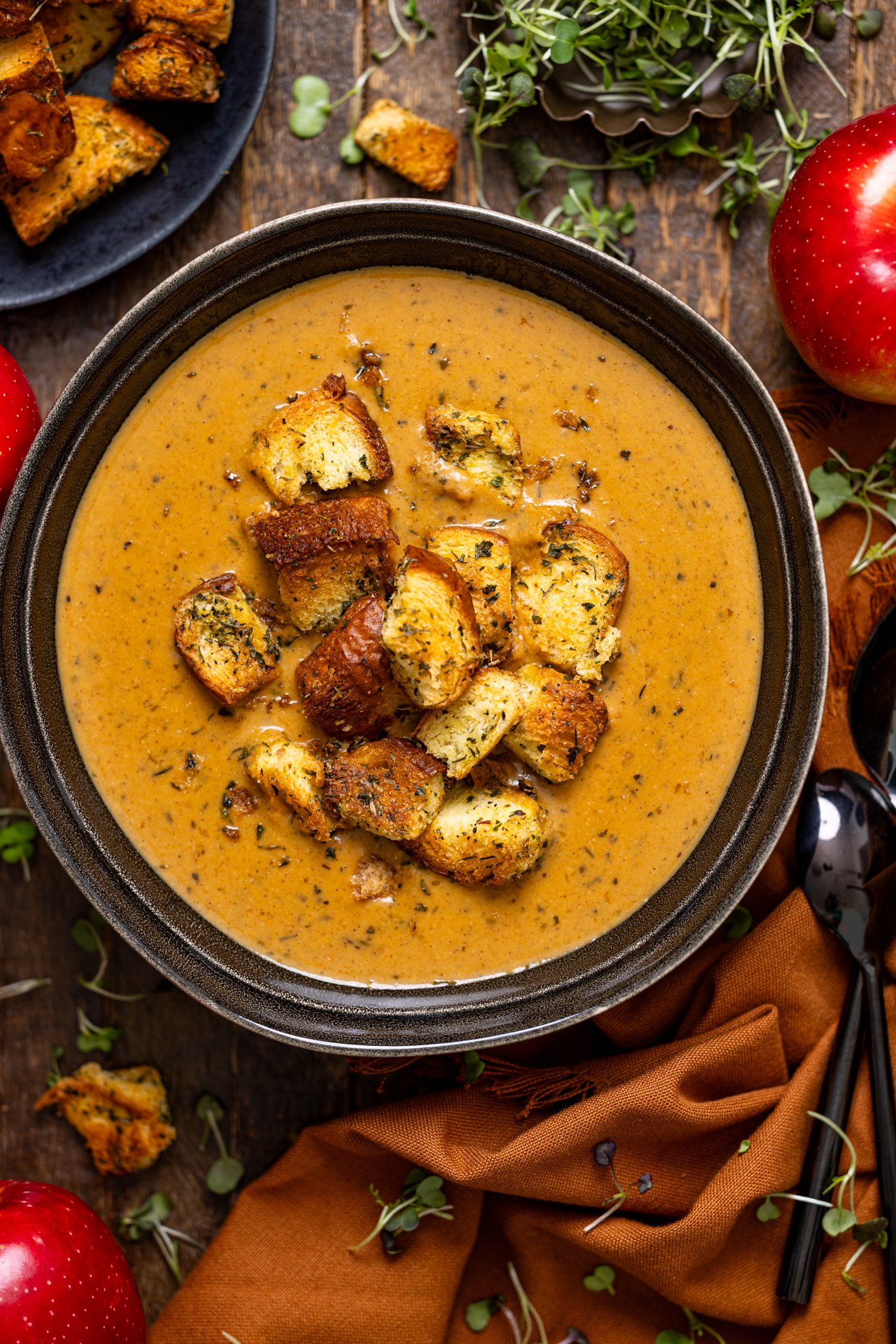 Creamy Roasted Apple Pumpkin Soup in a bowl on a brown wooden table with spoons.