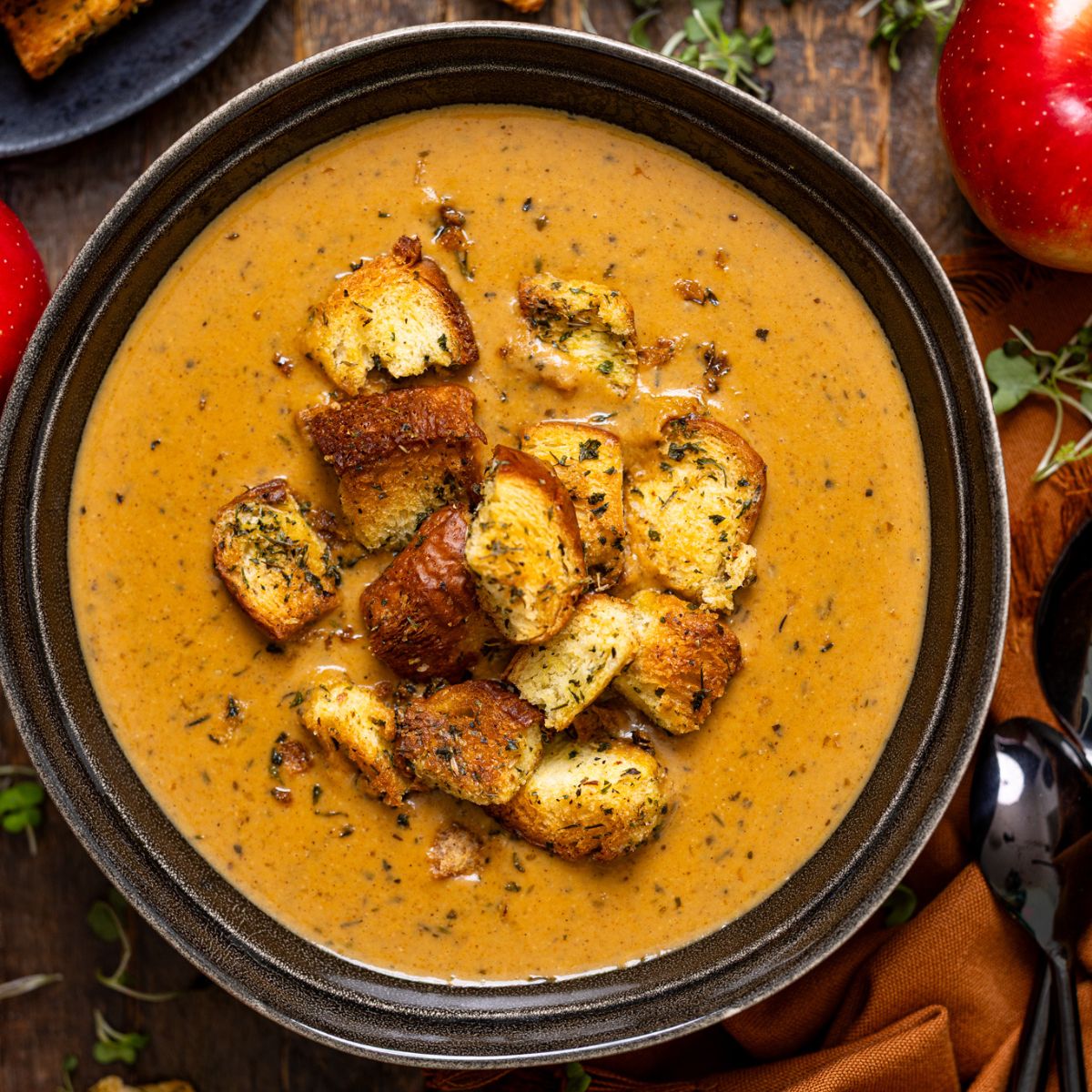 Creamy Roasted Apple Pumpkin Soup in a bowl on a brown wooden table with spoons.