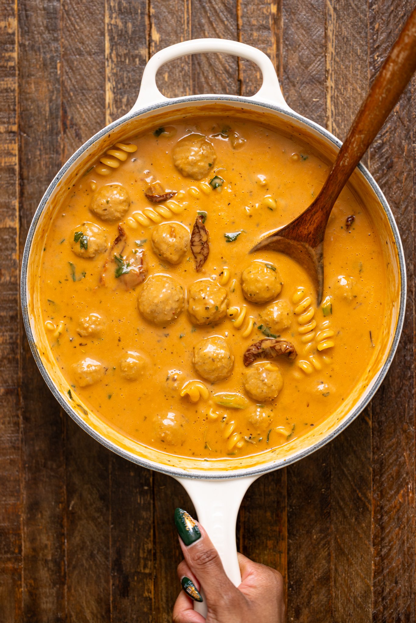 Hearty Tuscan 'Marry Me' Meatball Soup in a pot with a wooden spoon being held by woman hand.