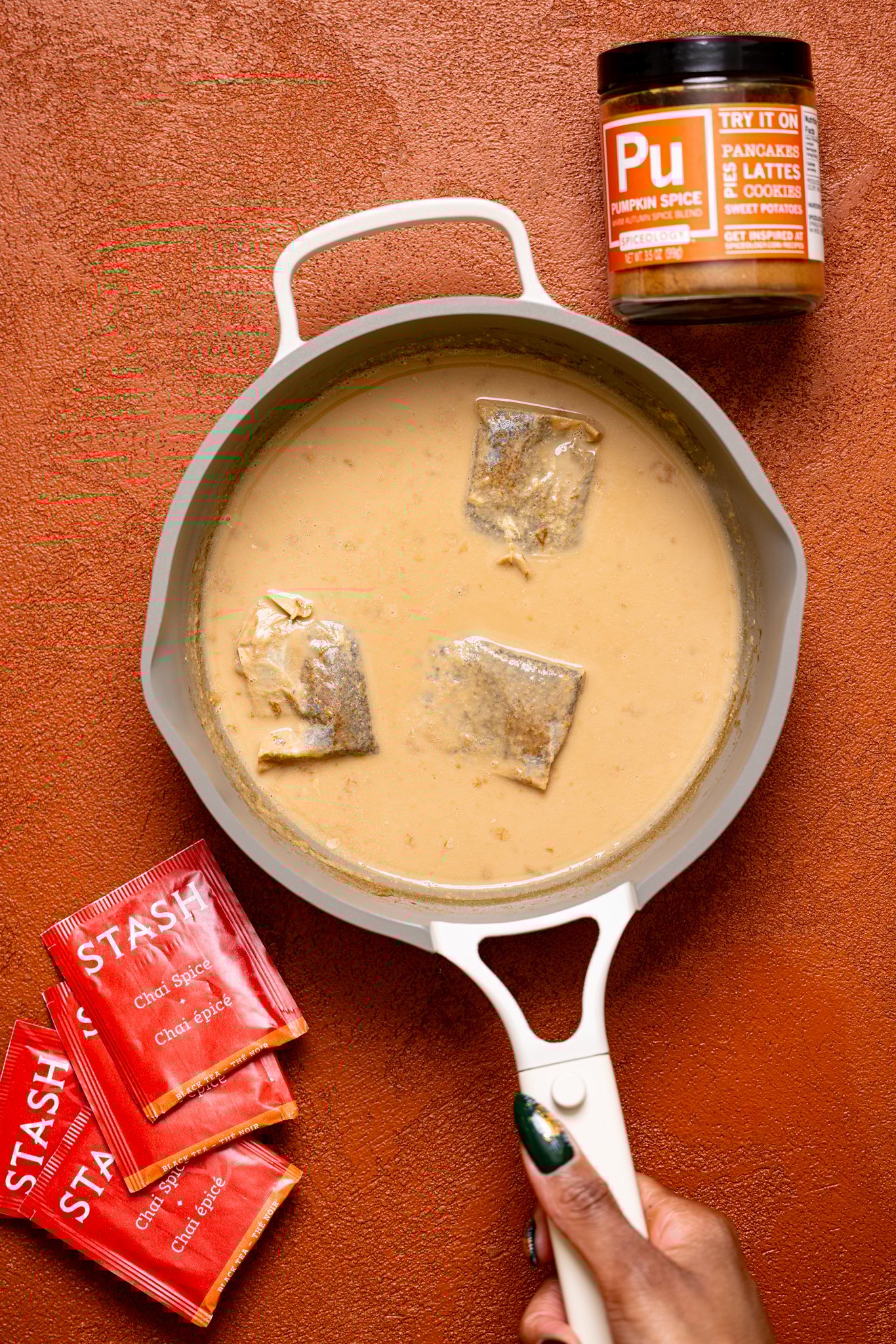 Chai tea mixture in a pot with tea bags being held by woman hand.