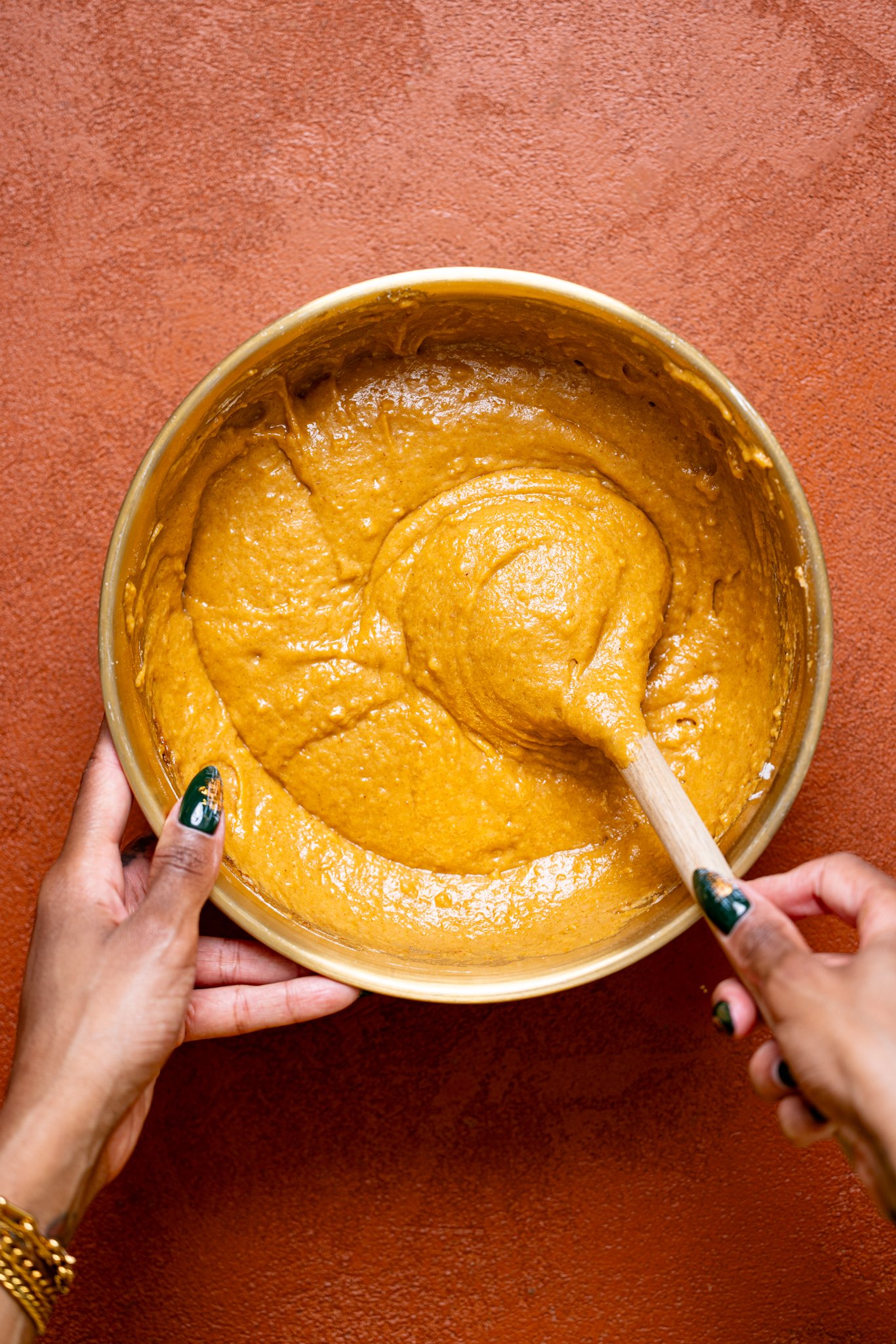 Pumpkin bread batter in a bowl being stirred with a wooden spoon by woman hands.