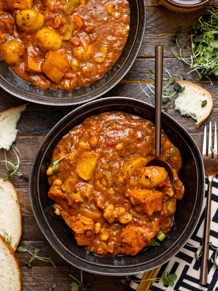 Hearty Vegan Sweet Potato Stew in two bowls with a spoon and drink.