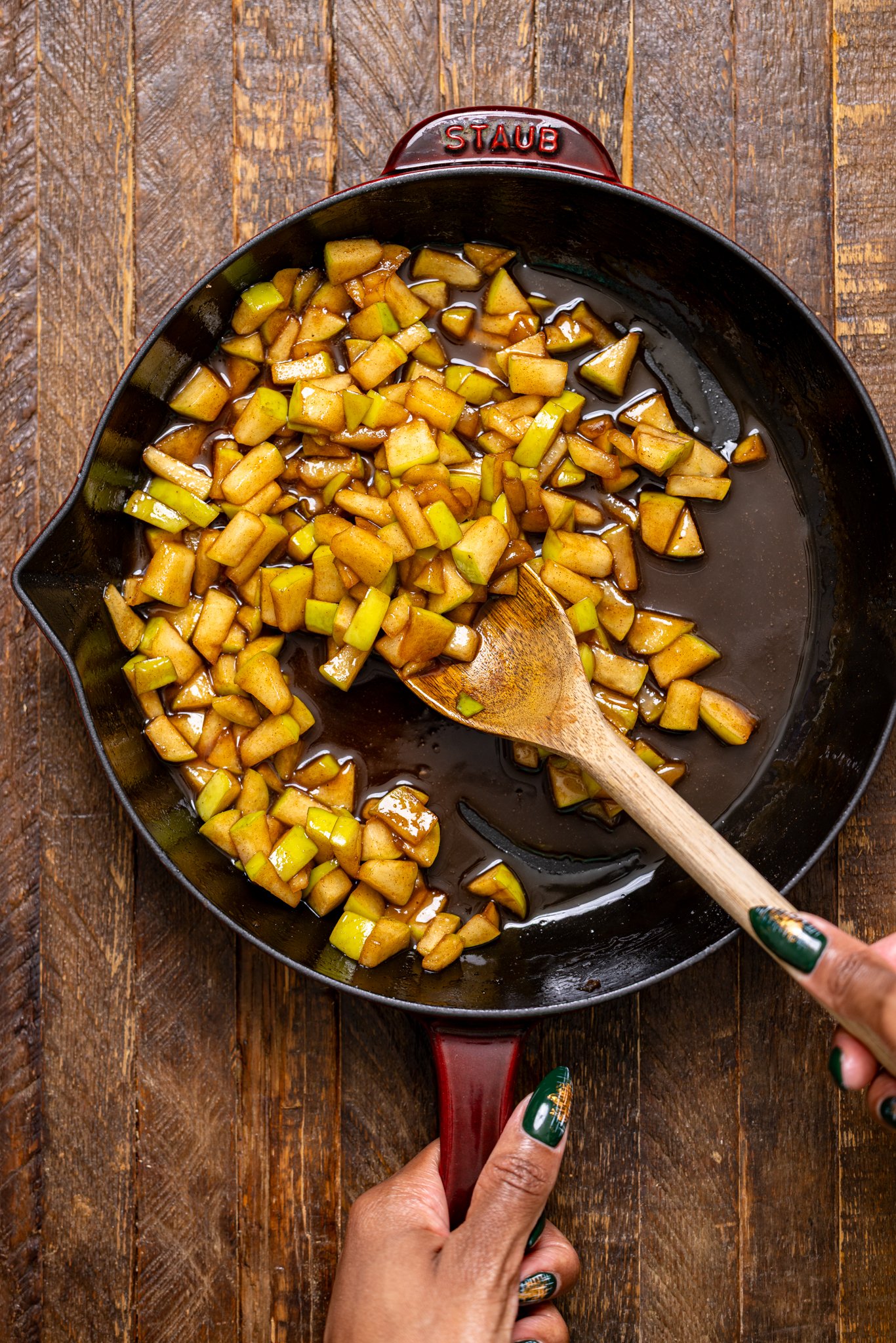 Sautéed diced apples in a skillet with a wooden spoon and woman hands.