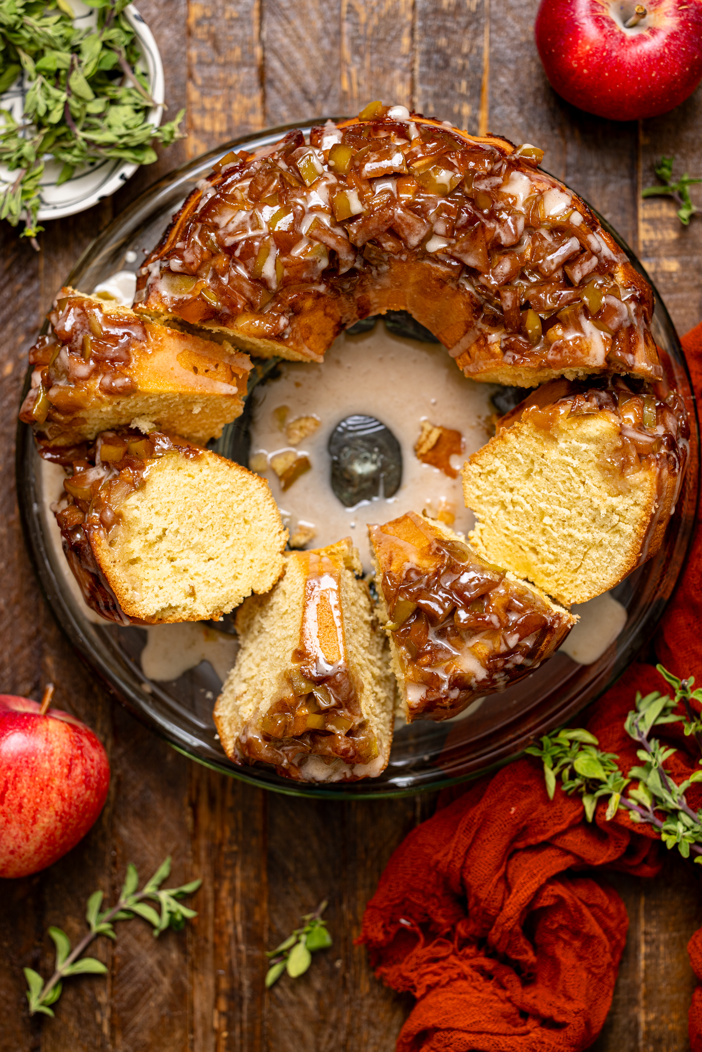 The Best Apple Pie Bundt Cake sliced on a cake stand with apples.