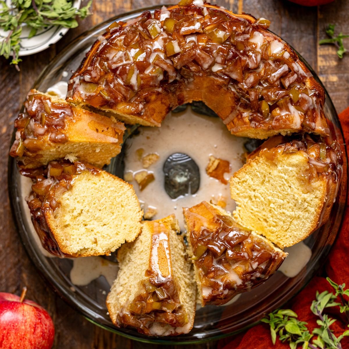 The Best Apple Pie Bundt Cake sliced on a cake stand with apples.