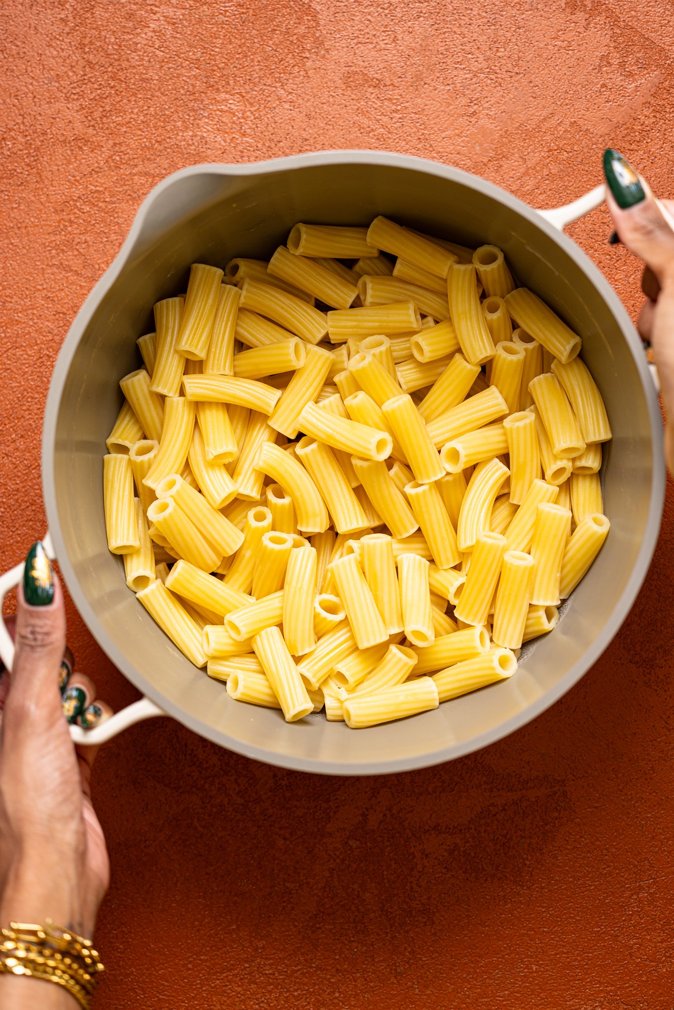 Cooked pasta in a pot being held by woman hands.