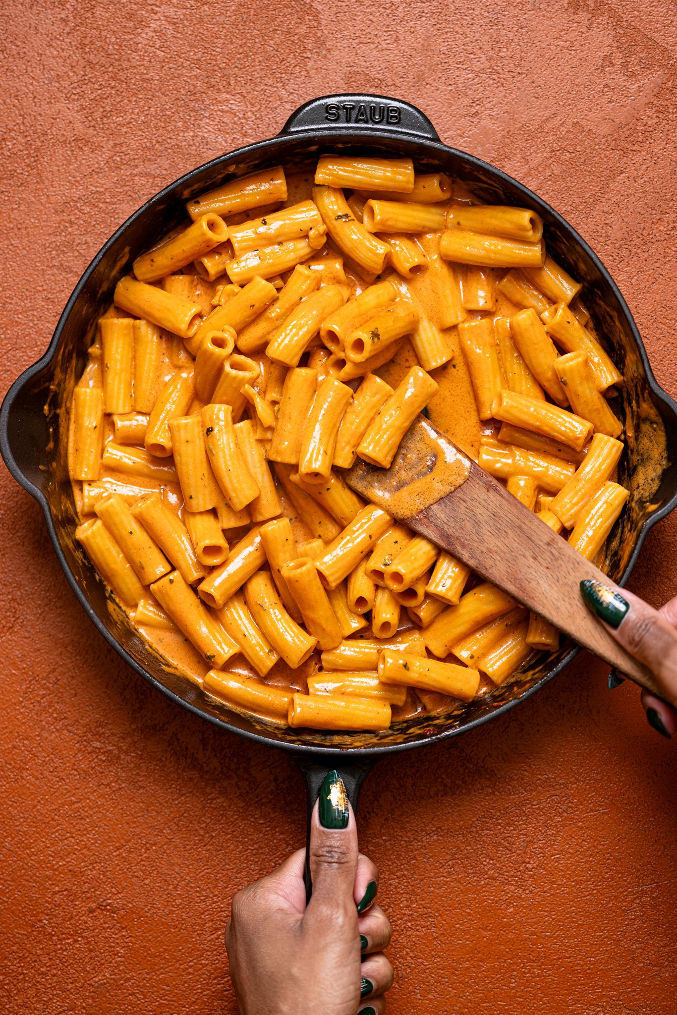 My Go-to Weeknight Alla Vodka Pasta in a skillet with a wooden spoon held with woman hands.